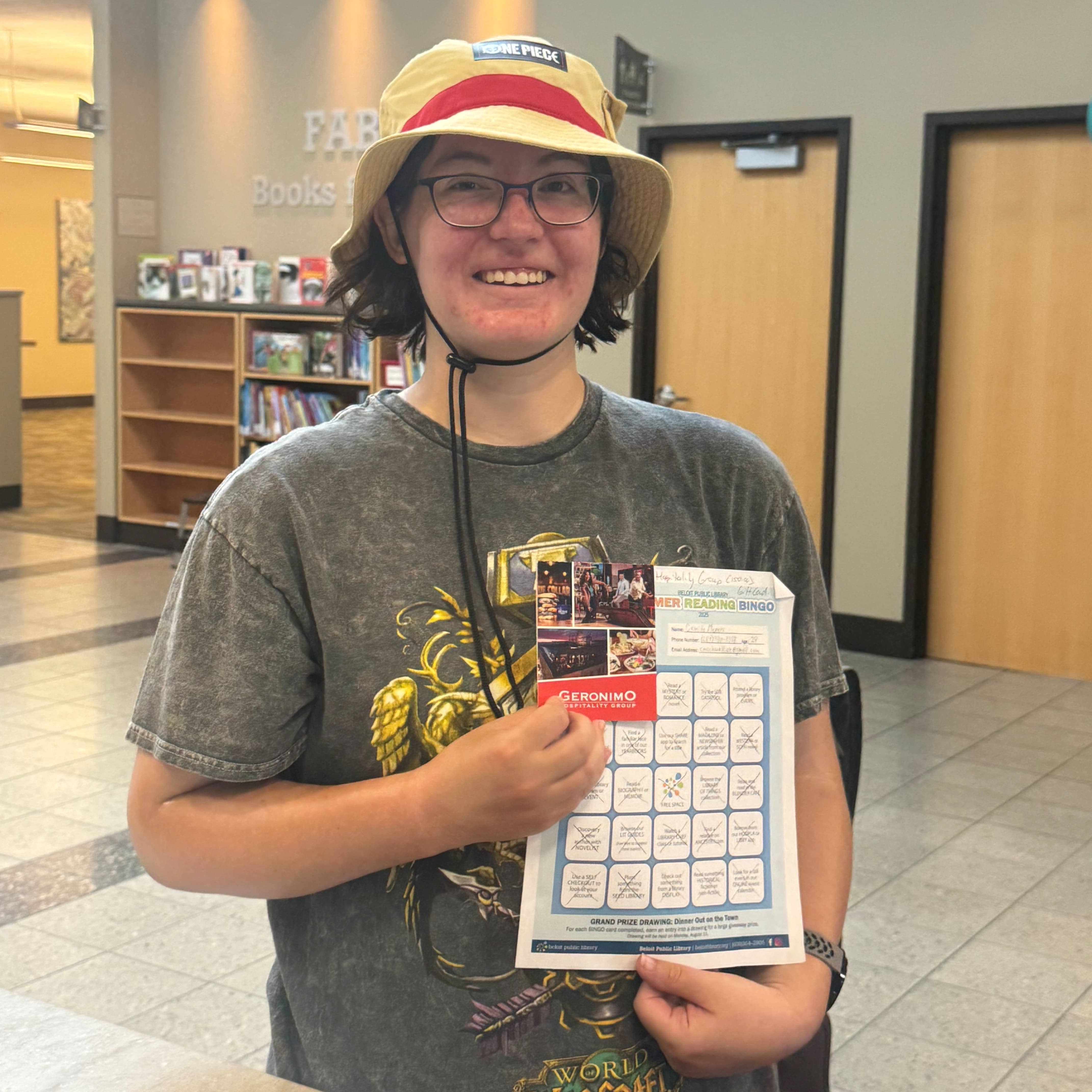 Smiling woman wearing glasses and a bucket hat, holding a bingo sheet and gift card
