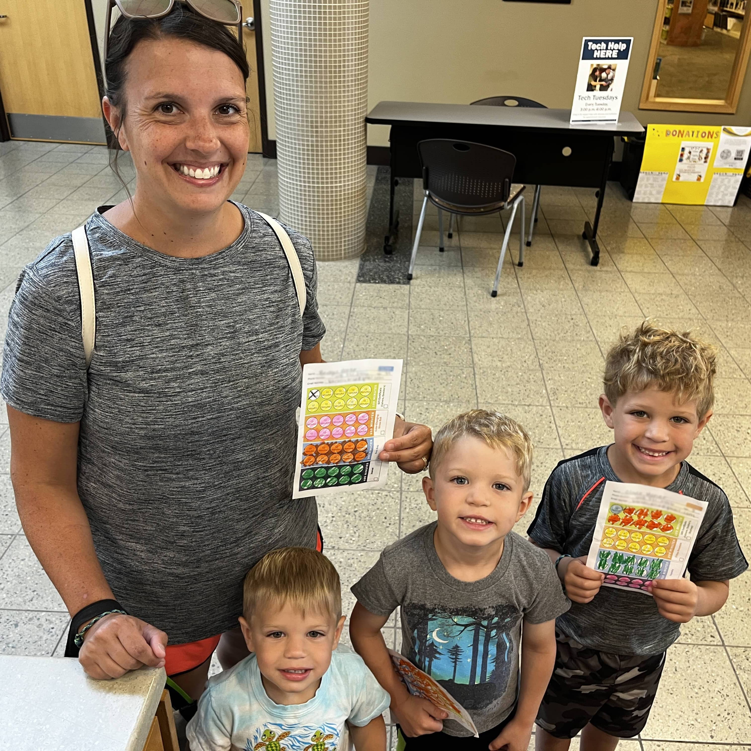 A smiling mother and her three smiling boys posing with their completed reading logs