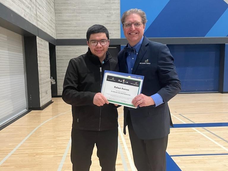 Young man in dark jacket standing next to a man in a suitcoat and bowtie holding a certificate in front of them
